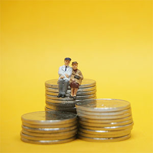 minature old couple sitting on top of pile of coins