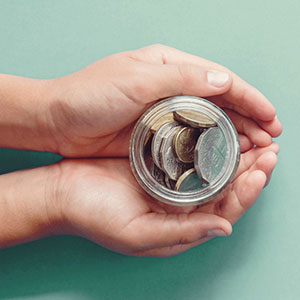 cupped hands holding a glass jar with coins inside