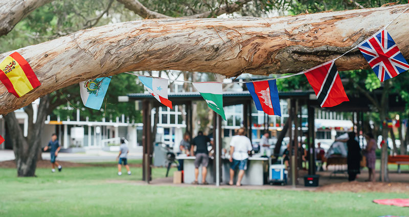 Flags of different countries in the tree branch with blured people in park doing barbecue together. Multicultural network, inclusivity concept