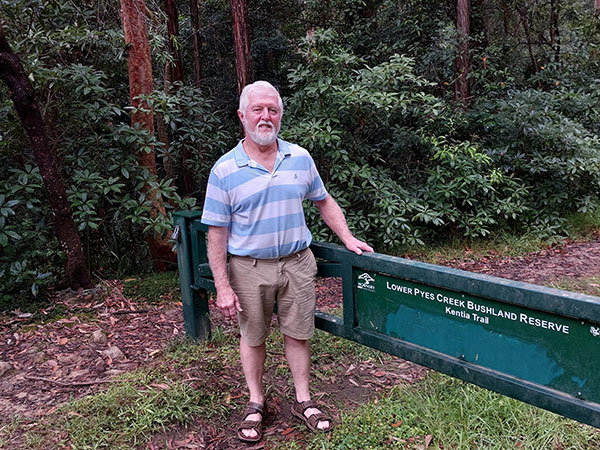 Man standing at bush trail with green fence