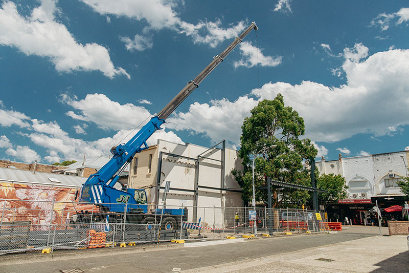 large blue crane behind steel fence with workers around