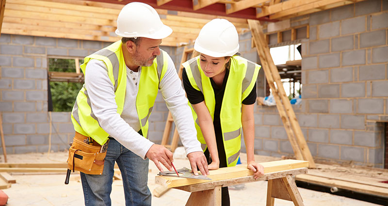 Carpenter With Female Apprentice Working On Building Site