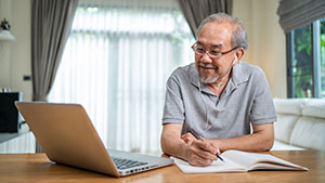 male in front of laptop with notepad and pen
